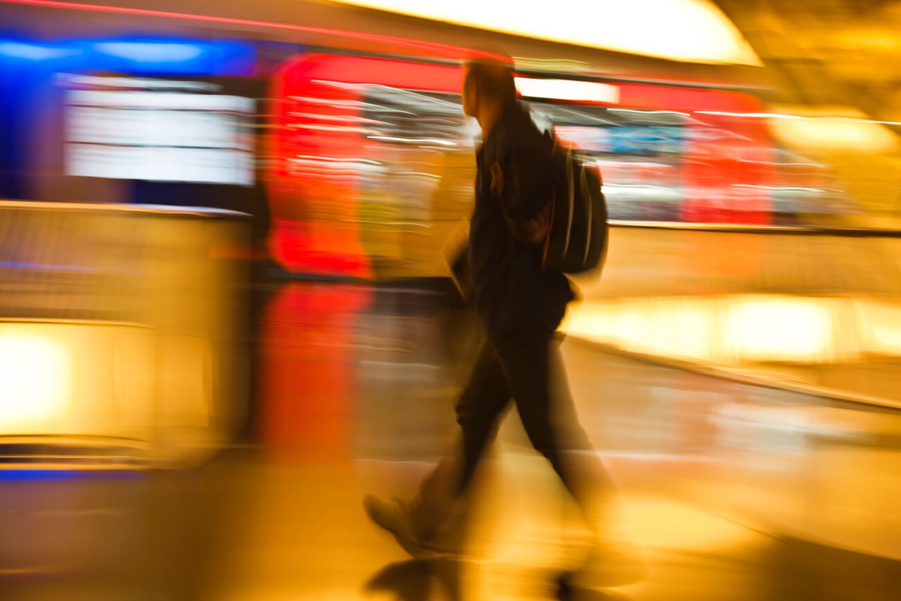 Man With Backpack Walking Past Illuminated Stores, Motion Blur